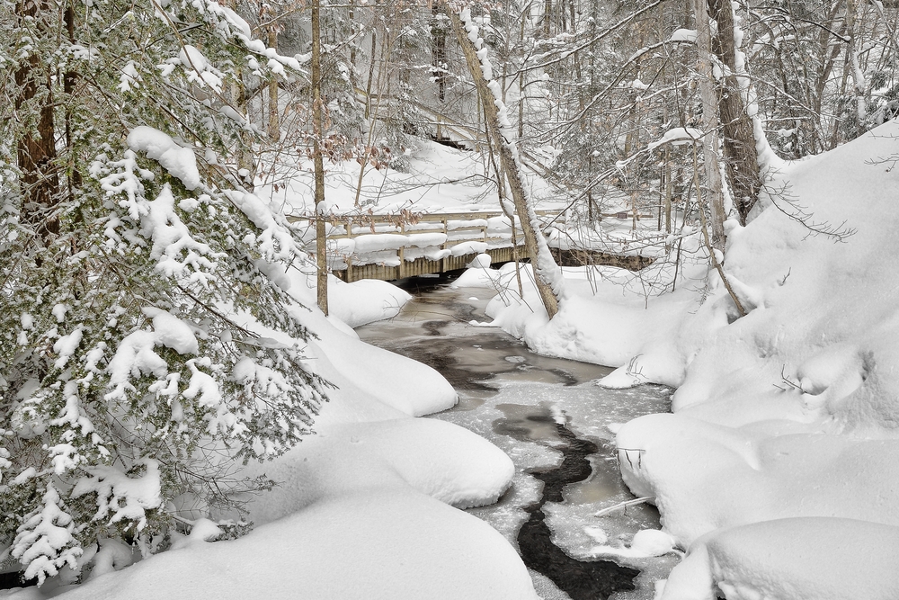 A bridge covers a partially frozen river, surrounded by snow-covered trees in Upper Peninsula, Michigan.