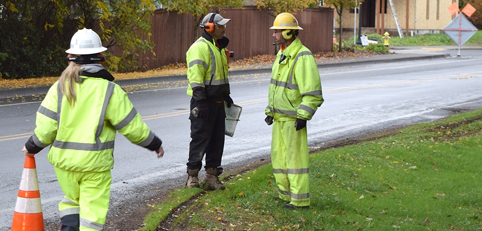 Three team members wearing Sonetics Wireless Headsets with hardhats at a road-side work site.