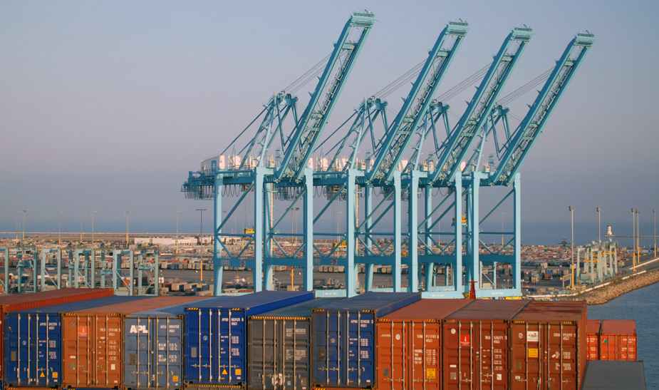 Cranes overlooking stacked shipping containers in a port.