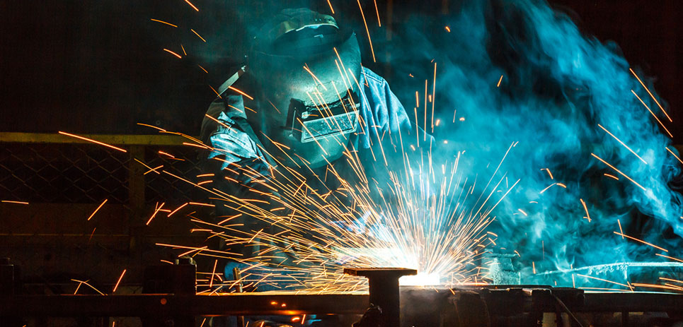 Welding sparks fly in an industrial work scene.