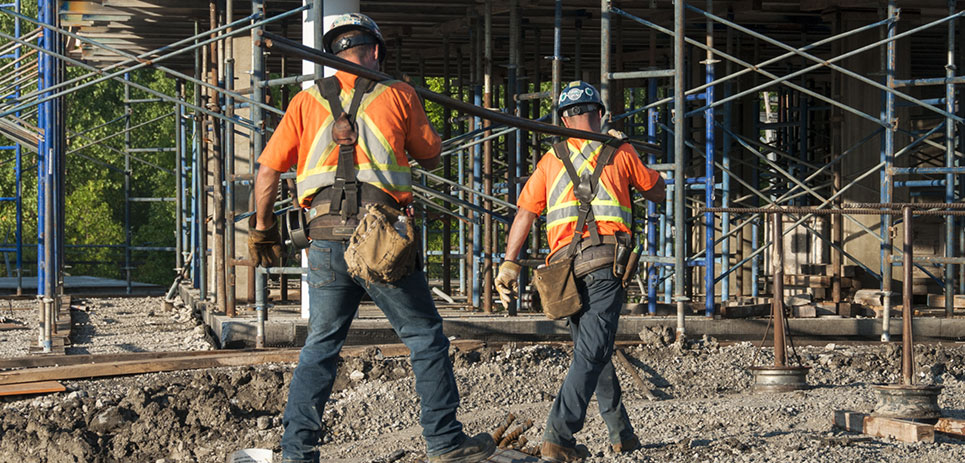 Two construction workers carry steel bar together.