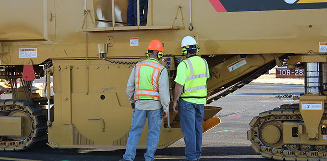 two workers standing in front construction equipment